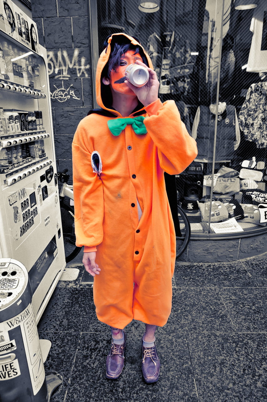 Japanese guy wearing pumpkin orange kigu PJs with some orange paint at his face on Halloween. 